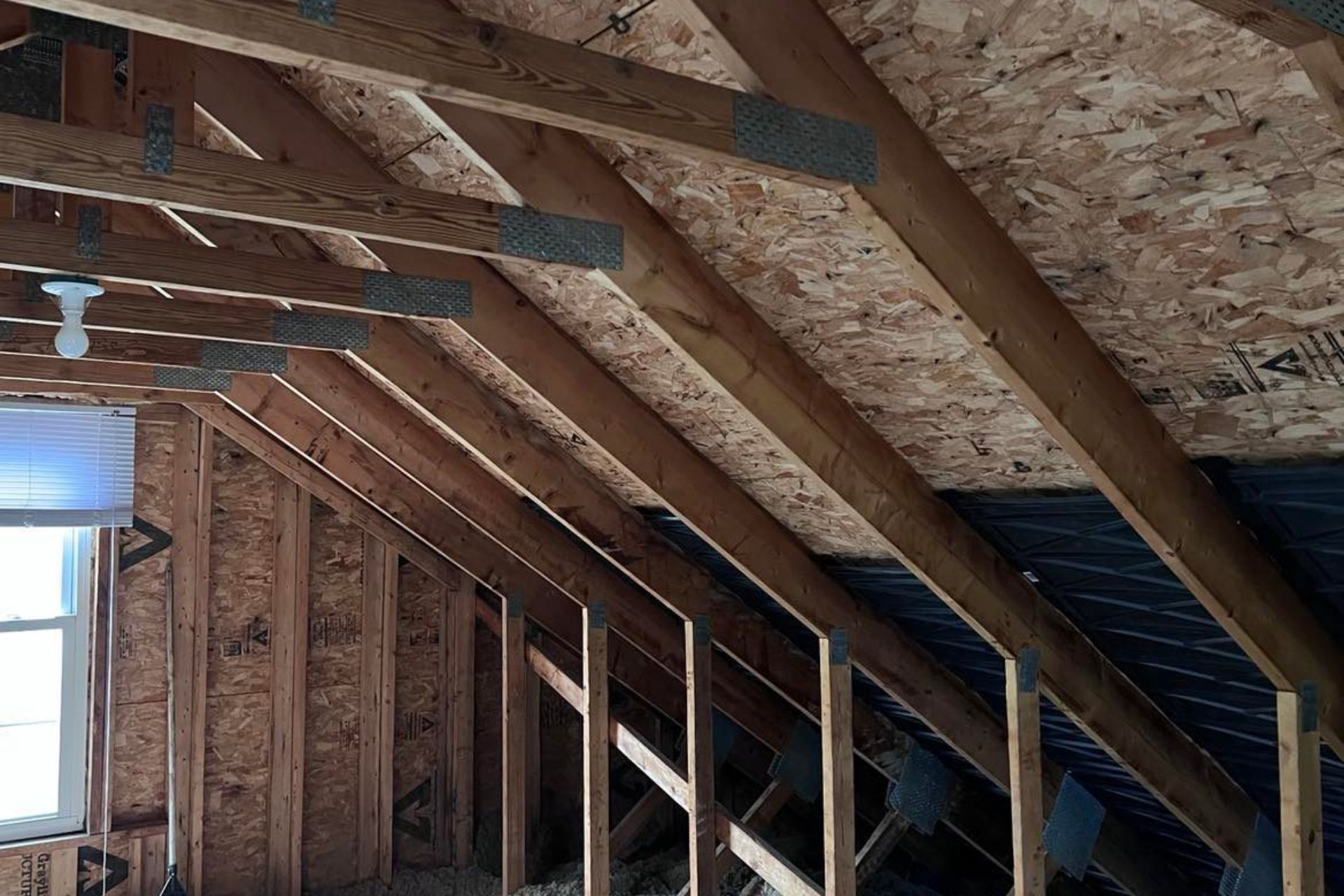 Attic interior featuring exposed wooden beams and insulation material on the ceiling and walls.