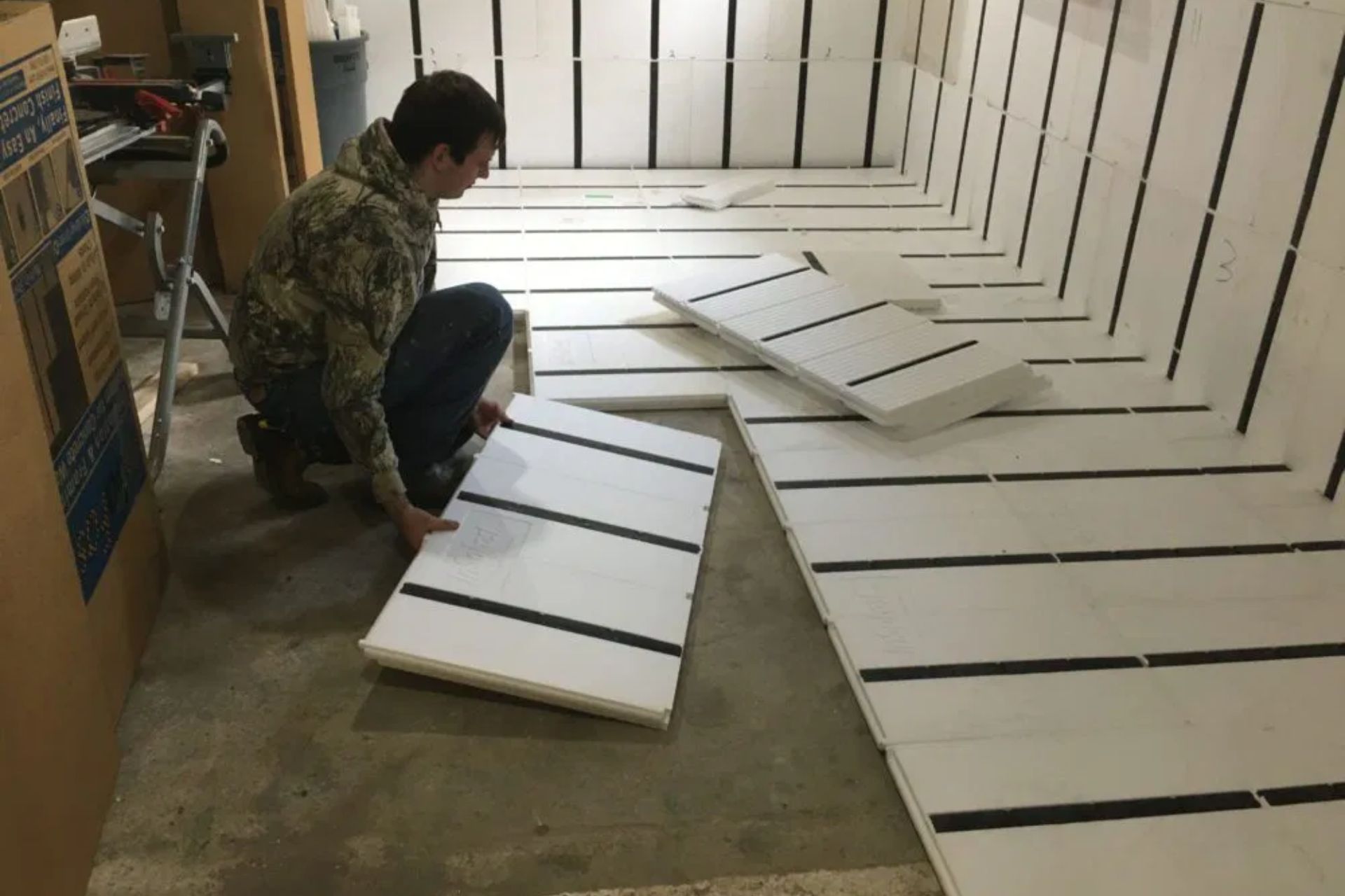 A person is arranging white panels with black stripes on the floor of a workspace.