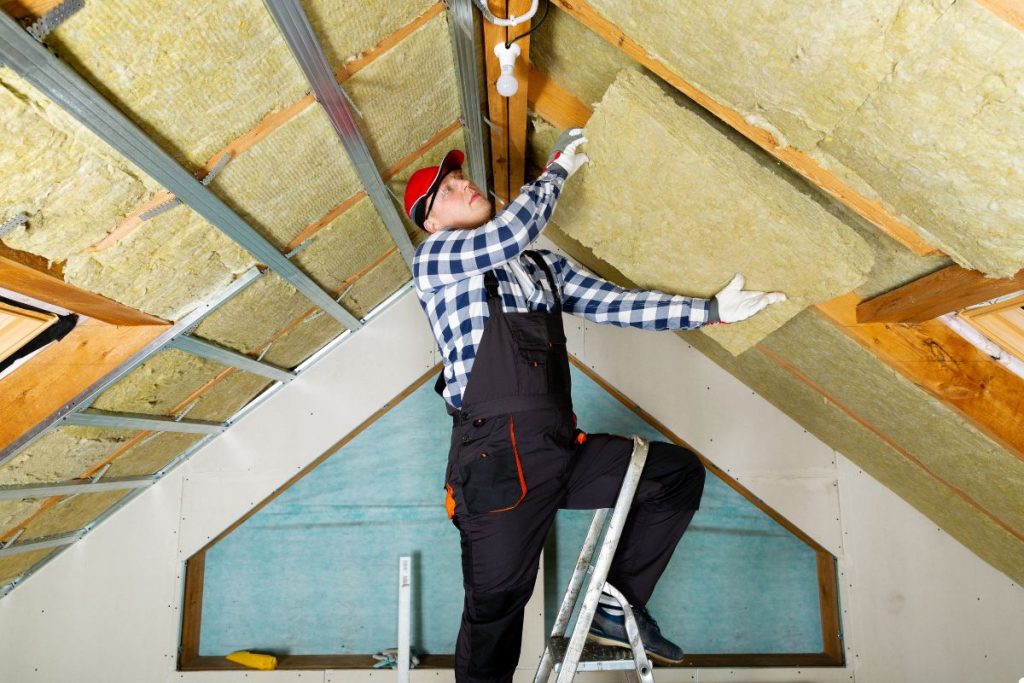 A man installs insulation on a roof, wearing safety gear and focused on his task.