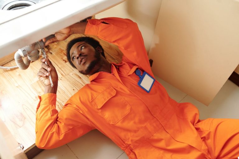 A man in an orange uniform is positioned on the floor, indicating repair issue.